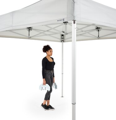 The woman carries the 28 kg base plate to the folding gazebo.